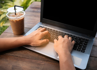 Close up Woman hand Using a  laptop with blank screen on wooden table at the backyard. Working on weekend concept.