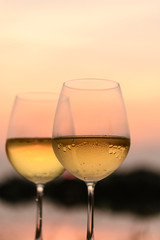 A romantic dinner in summer on a beach at sunset with two glasses of white wine