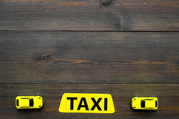 Taxi concept. Yellow service sign text taxi near car toy on dark wooden background top view copy...