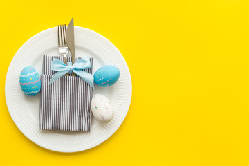 Fototapeta na wymiar Easter table decoration. Plate, cutlery, painted eggs on yellow background top view copy space