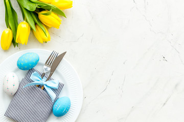 Festive traditional Easter dinner concept. Tableware, painted eggs, tulips flowers on white stone...