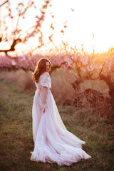 Fototapeta premium Beautiful young girl under the flowering pink spring tree