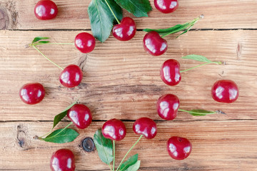 Naklejka na ściany i meble Ripe cherry with green leaves on wooden background. Fruit background.