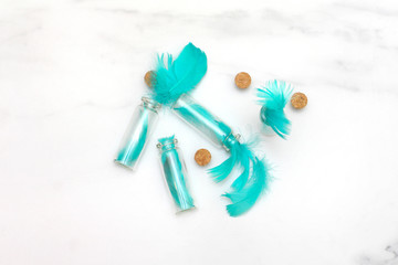 Composition of feathers turquoise color and bottles on the marble surface. Flat lay, top view