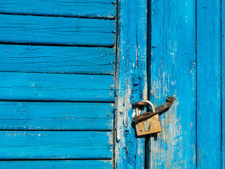 The wooden door with peeling blue paint is locked with a padlock.