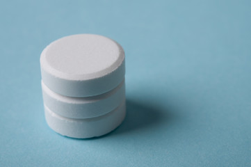 stack of white round pills with shadow on blue background; medicine dosage and medical treatment concept