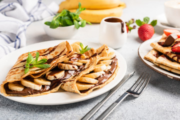Chocolate hazelnut spread and banana filled crepes on plate. Tasty crepes or blini with sweet sauce...