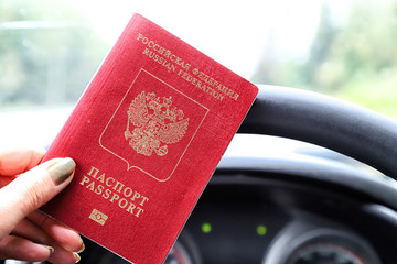 Russian passport in the hand of woman and and the steering wheel of a car with a blurred landscape...