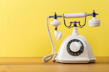  old white telephone on wooden table with color wall background