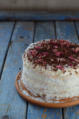 Delicious coconut layer cake - biscuit and cream on coconut cream, decorated with grated chocolate and candied rose petals.
