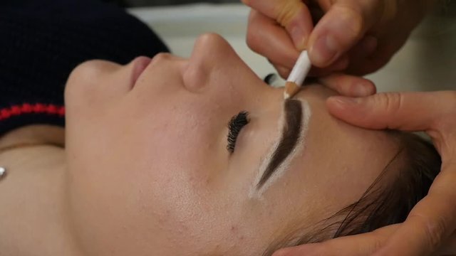tattoo master prepares the client's eyebrows to permanent makeup, makes markup