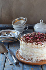 Delicious coconut layer cake - biscuit and cream on coconut cream, decorated with grated chocolate and candied rose petals.
