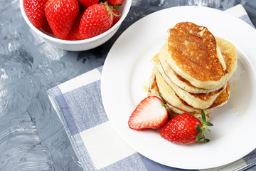 Pancakes on a plate and strawberries on a gray background