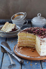 Delicious coconut layer cake - biscuit and cream on coconut cream, decorated with grated chocolate and candied rose petals.