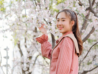 Outdoor portrait of beautiful young Chinese girl in red shirt posing among pink blossom cherry tree brunch in spring garden, beauty, summer, emotion, expression and people concept. 
