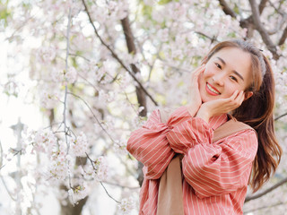 Outdoor portrait of beautiful young Chinese girl in red shirt posing among pink blossom cherry tree brunch in spring garden, beauty, summer, emotion, expression and people concept. 