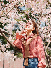 Outdoor portrait of beautiful young Chinese girl in red shirt posing among pink blossom cherry tree brunch in spring garden, beauty, summer, emotion, expression and people concept. 
