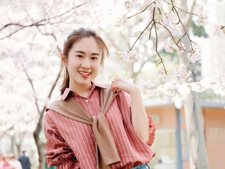 Outdoor portrait of beautiful young Chinese girl in red shirt posing among pink blossom cherry tree brunch in spring garden, beauty, summer, emotion, expression and people concept. 