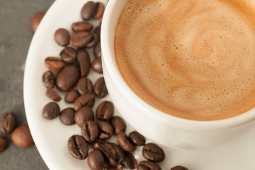 Cup of coffee with perfect cream and coffee beans on gray background