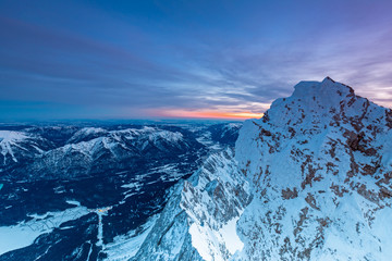 Fototapeta premium Tagesanbruch auf dem Gipfel der Zugspitze mit Blick auf das erleuchtete Garmisch Partenkirchen und ins Loisachtal