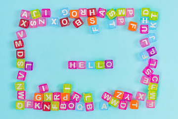 Hello inscription made of colorful cube beads with letters. Festive blue background concept with copy space.