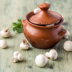 Small raw champignon mushrooms and a clay pot on an old wooden table.
