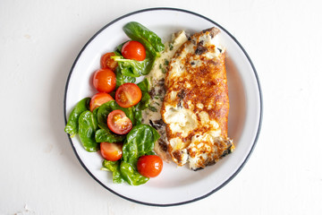 Omelet with mushrooms, salad with cherry tomatoes and spinach, on a light background. Healthy eating concept. Close-up.