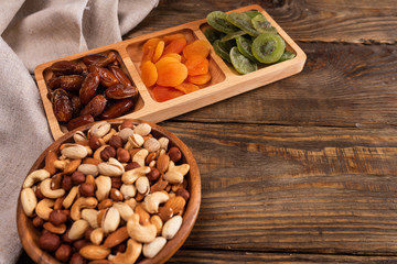 Fototapeta na wymiar Dates, dried apricots and kiwis in a Compartmental dish and assortment of nuts in wooden bowl on a dark wooden table.