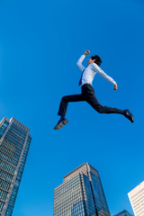 Fototapeta na wymiar 青空とオフィスビル群をバックにジャンプする若いビジネスマン1人。ビジネス、努力、成功、活発、エネルギッシュ、イメージ