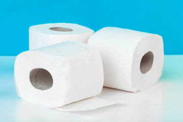 Three toilet paper rolls isolated on white table with blue background
