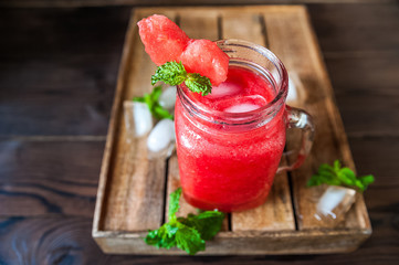 Watermelon refreshing smoothie in a jar close-up and copy space. Watermelon smoothie with a heart of watermelon, mint, ice on a textured red brick wall.