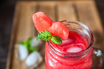 Watermelon refreshing smoothie in a jar close-up and copy space. Watermelon smoothie with a heart of watermelon, mint, ice on a textured red brick wall.