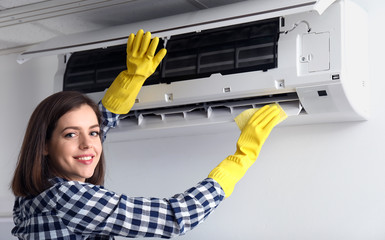 Young woman cleaning air conditioner at home
