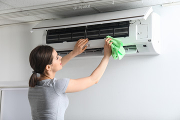Young woman cleaning air conditioner at home