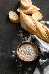 Cut French bread with flour on grey background