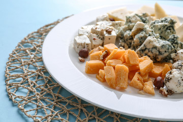 Plate with assortment of tasty cheese on color background