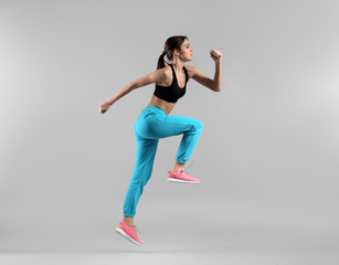 Fototapeta na wymiar Sporty young woman jumping against light background