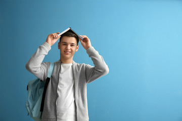 Schoolboy with book on color background