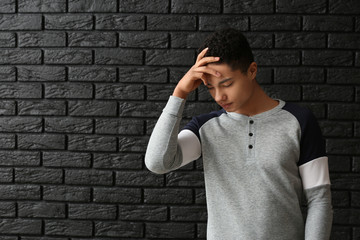 Sad African-American boy after failing school test on dark background