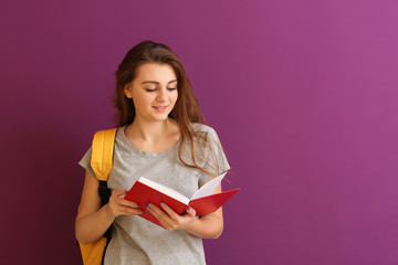 Schoolgirl with book on color background