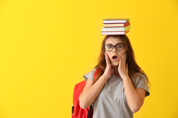 Shocked schoolgirl with books on color background