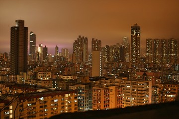 Skyscrapers, high-rise and low-rise buildings and roads at night time in Kowloon, Hong Kong illuminated with neon lights and with strong light pollution in cloudy, rainy night sky