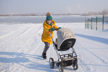 Young woman in yellow down jacket pushes baby carriage and smiles outside