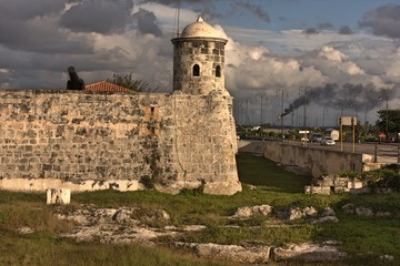 Fototapeta na wymiar Lookout tower with black cannon in background and factory spewing black smoke under cloudy blue sky