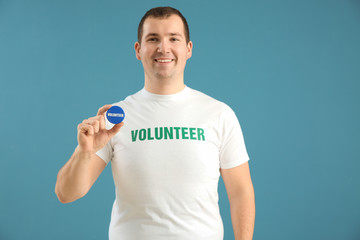 Young male volunteer with badge on color background