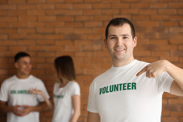Young male volunteer and his team against brick wall