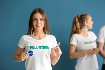 Young female volunteer and her team on color background