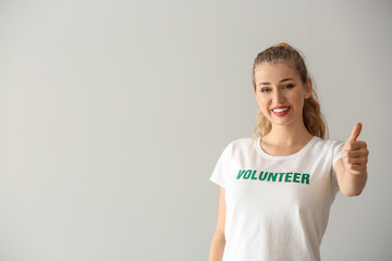 Young female volunteer showing thumb-up on light background