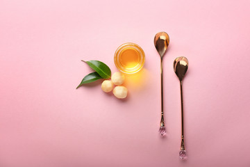 Spoons and macadamia oil on color background