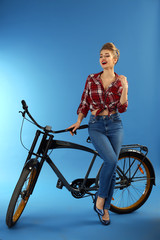 Fototapeta na wymiar Beautiful pin-up woman with bicycle on color background